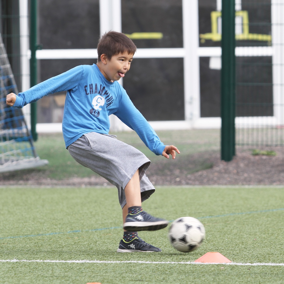 Poika pujottelee jalkapallon kanssa. Hänellä on päällään sininen paita.