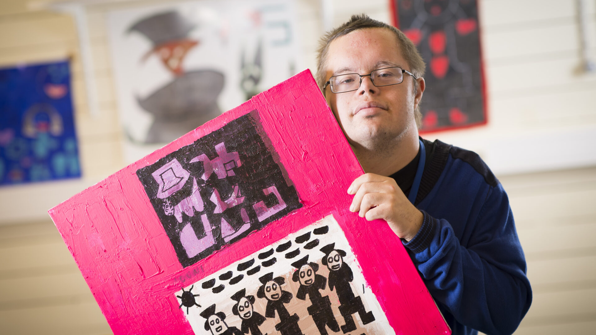 Mies pitää käsissään maalausta, jossa on ihmishahmoja pinkillä taustalla.