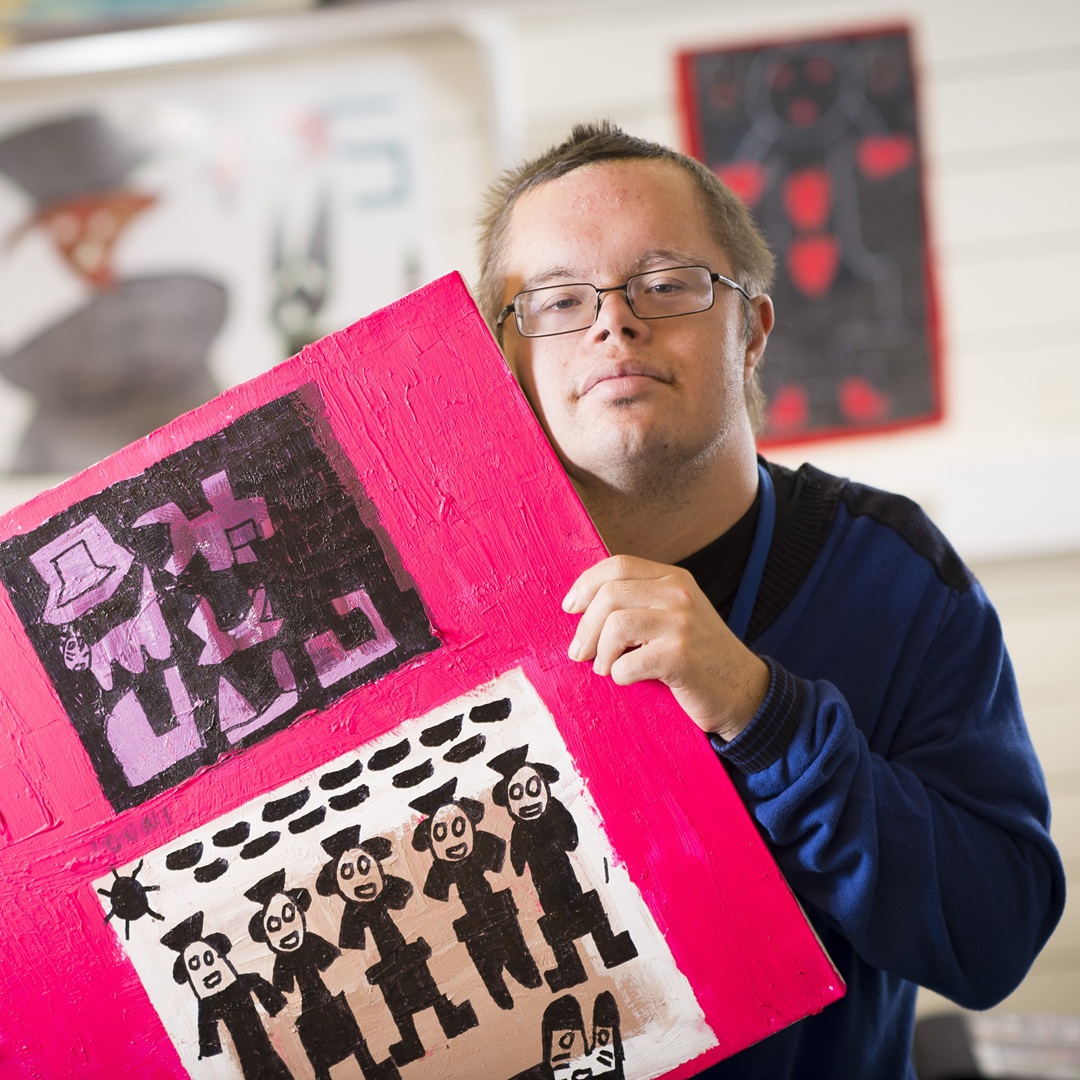 Mies pitää käsissään maalausta, jossa on ihmishahmoja pinkillä taustalla.