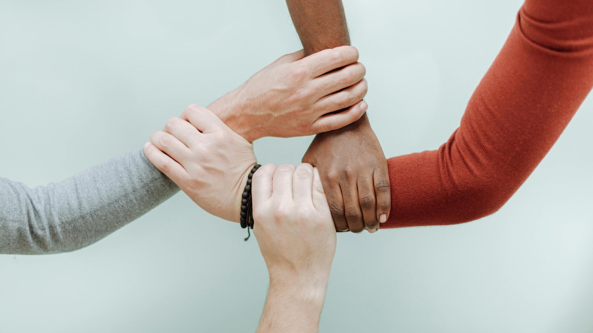 Neljä kättä pitää toisiaan ranteista kiinni.