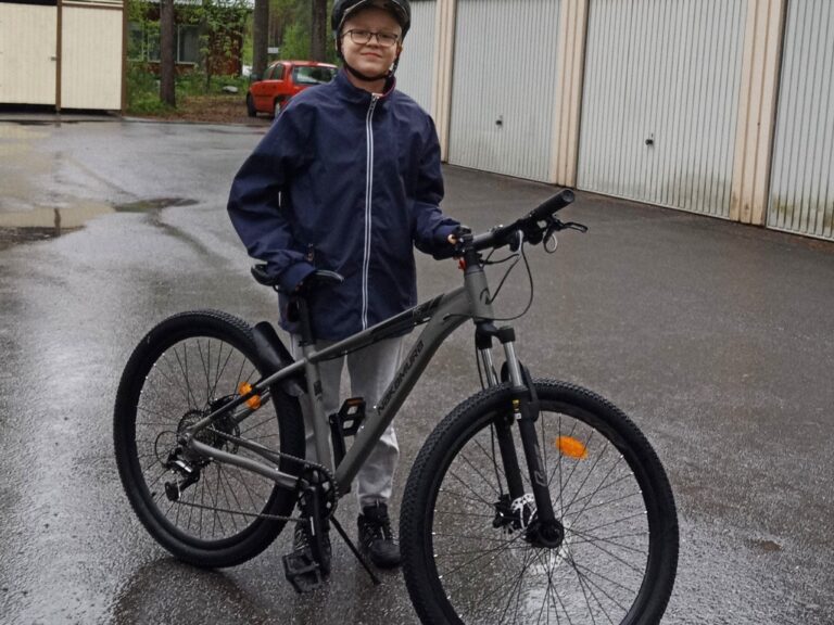 Iloinen poika polkupyörän vieressä.