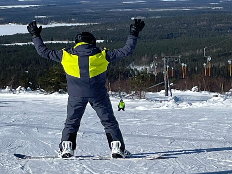 Lumilautailija pitää käsiään ylhäällä rinteen huipulla.