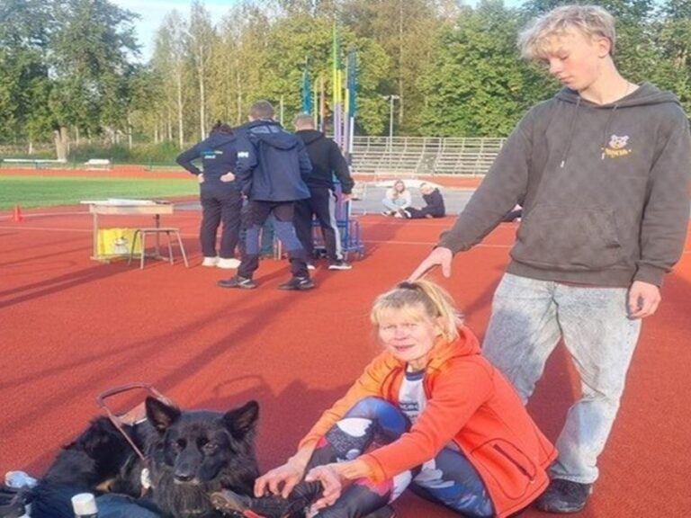 Nainen urheilukentällä. Hänen takanaan on nuori mies.