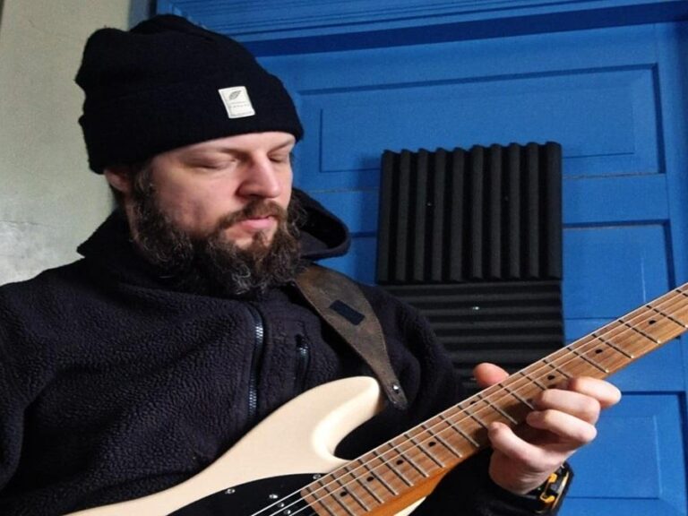 Mies soittaa kitaraa tummassa asussa.