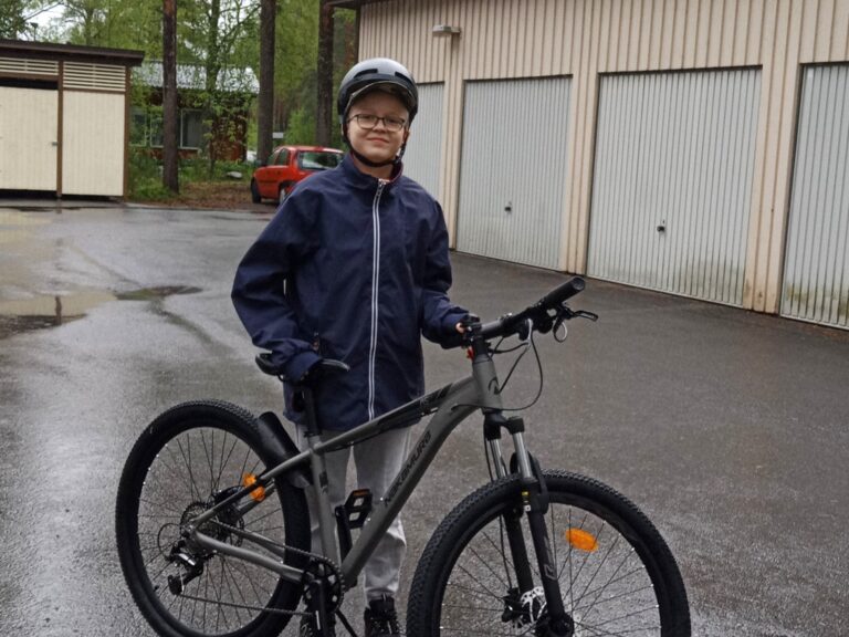Iloinen poika polkupyörän vieressä.