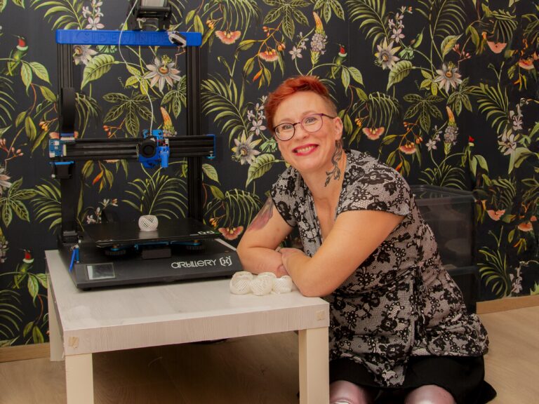 Proteeseja käyttävä nainen istuu 3D-tulostimen vieressä.