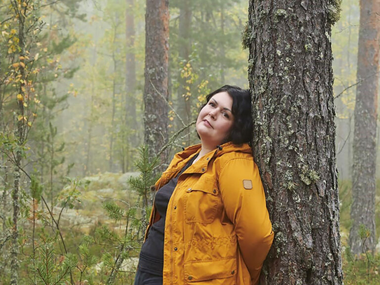 Marketta Moksi nojaa metsässä selkäänsä puunrunkoa vasten